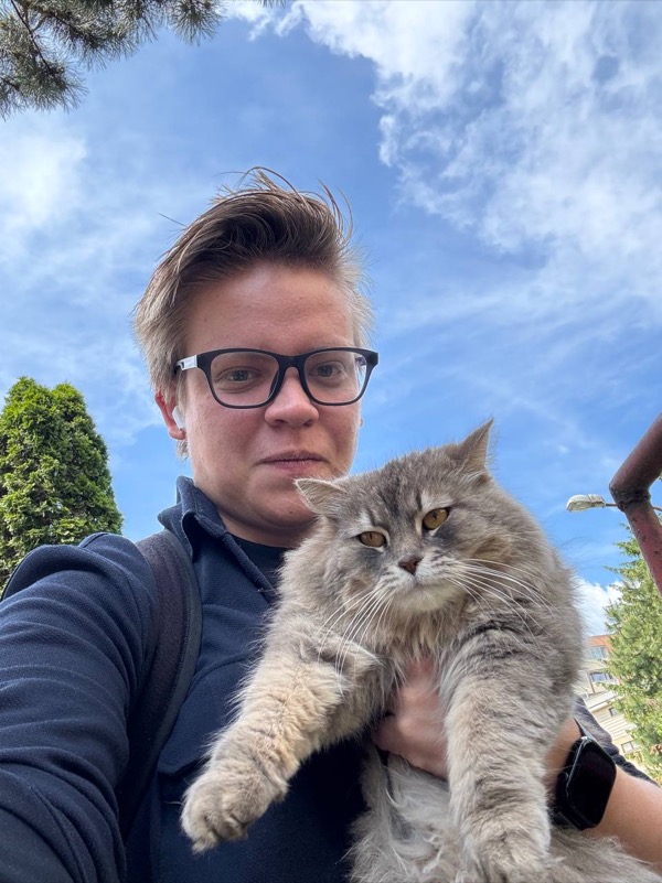 Artem Efremenko taking a selfie with a large fluffy grey cat under a blue sky.