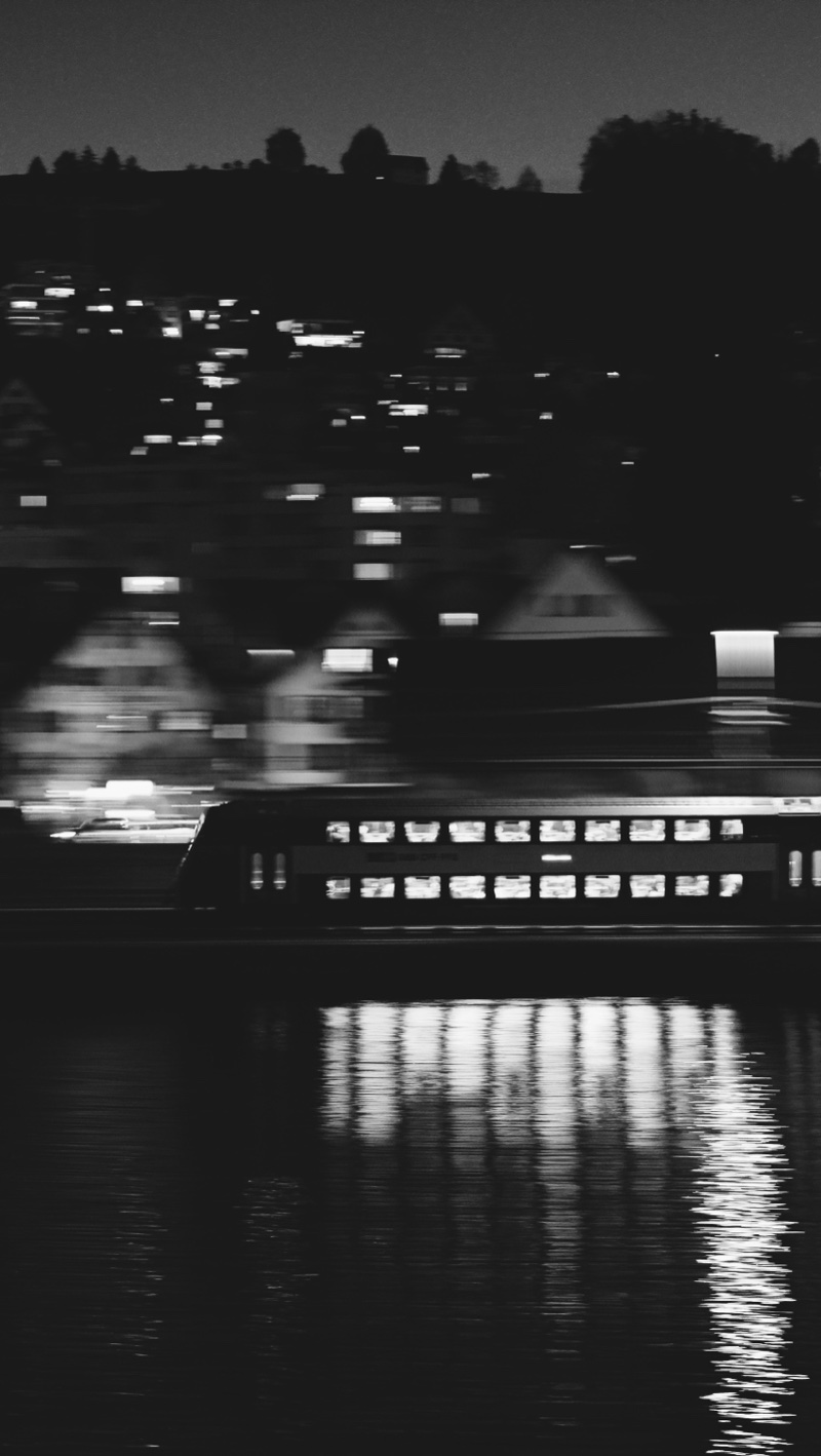 Black and white night view of a lit lake boat, its reflection on the water.