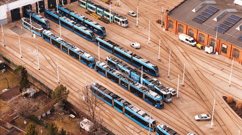 Blue trams parked in a depot yard next to a brick shed with solar panels.