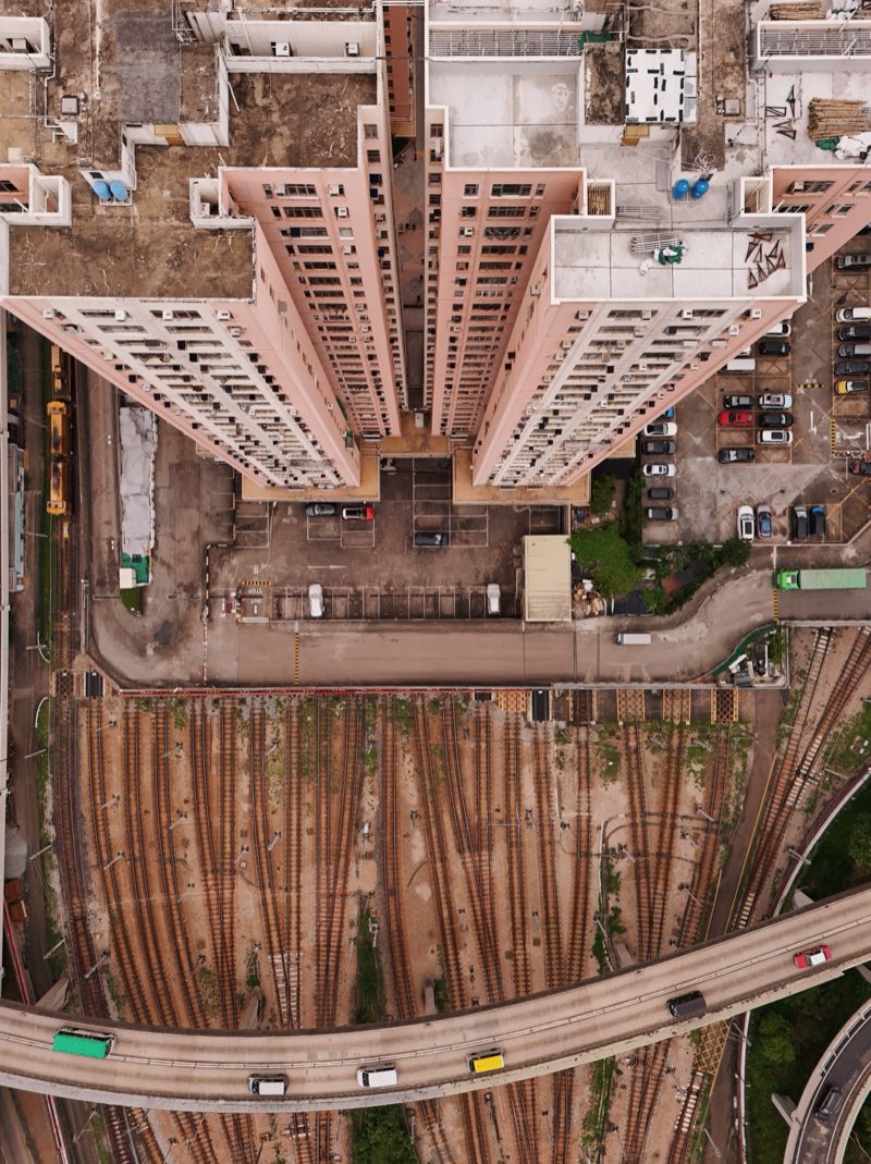 Looking straight down on two high-rise towers, with a rail yard and a curving flyover below.