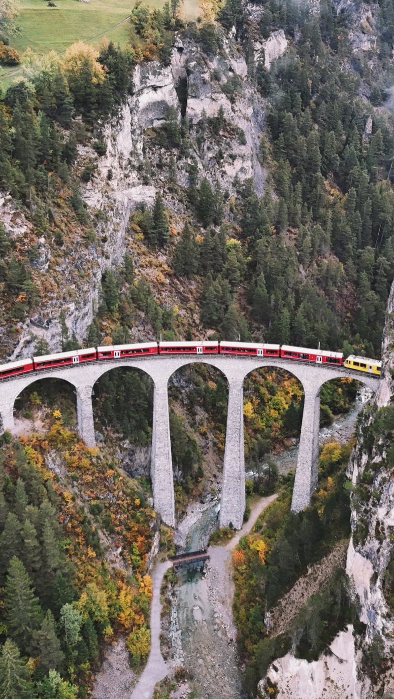 Red train on a tall viaduct high above a narrow gorge.