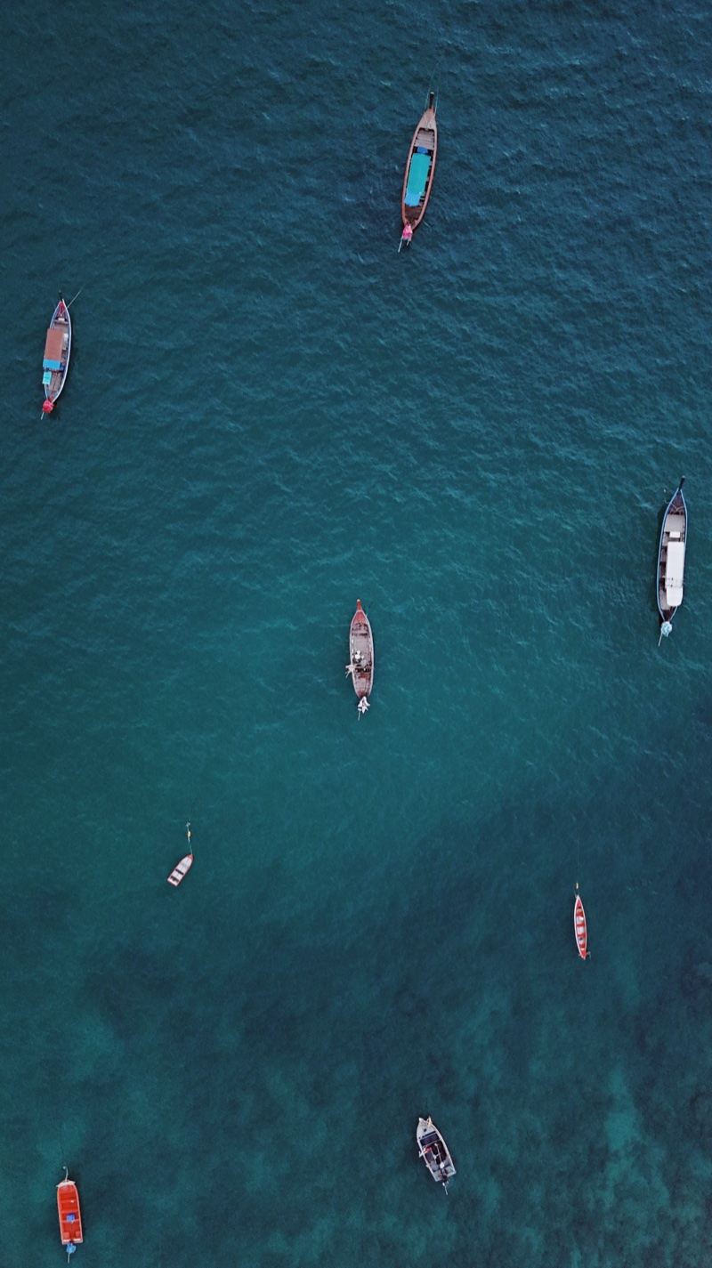 Small boats scattered on deep blue-green water, seen from above.