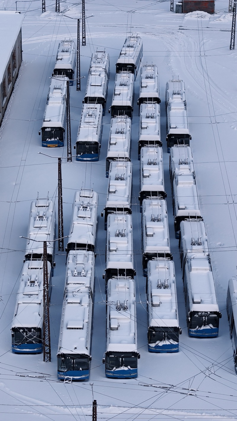 Snow-covered trolleybuses parked in rows, seen from above.