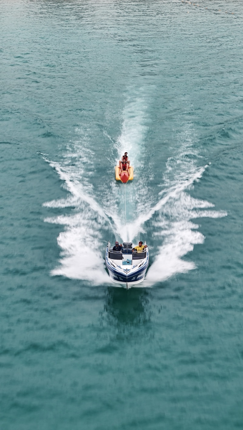 Speedboat towing a rider across turquoise water, leaving a white wake.