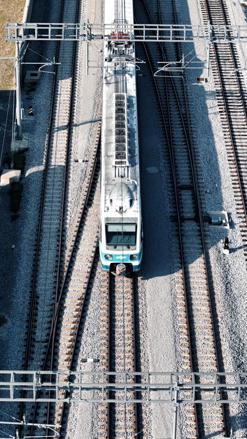 Train seen from directly above on multi-track railway under overhead line gantries.