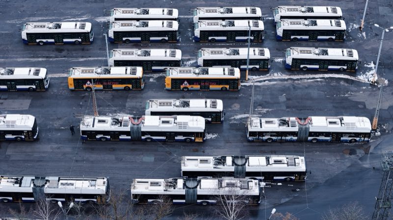 White and yellow buses parked in rows in a snowy depot.