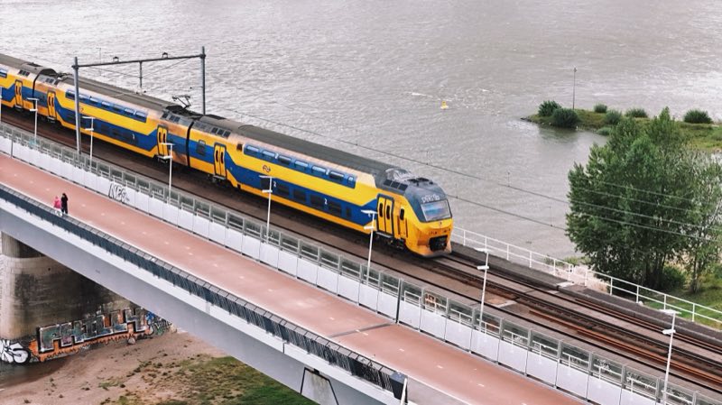 Yellow and blue double-deck train crossing a bridge over a wide river.
