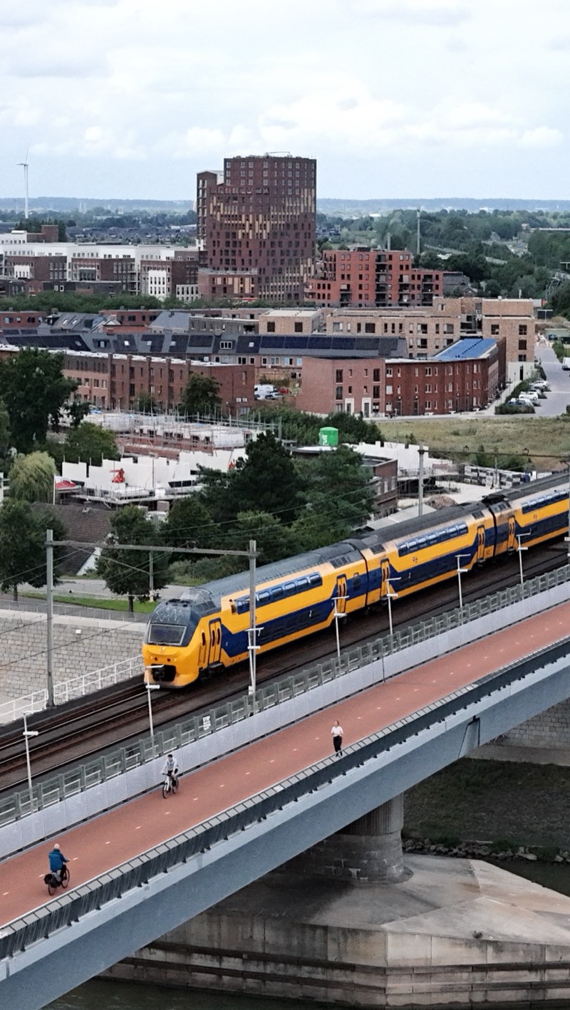 Yellow and blue double-deck train on a viaduct, brick buildings and a round tower behind.