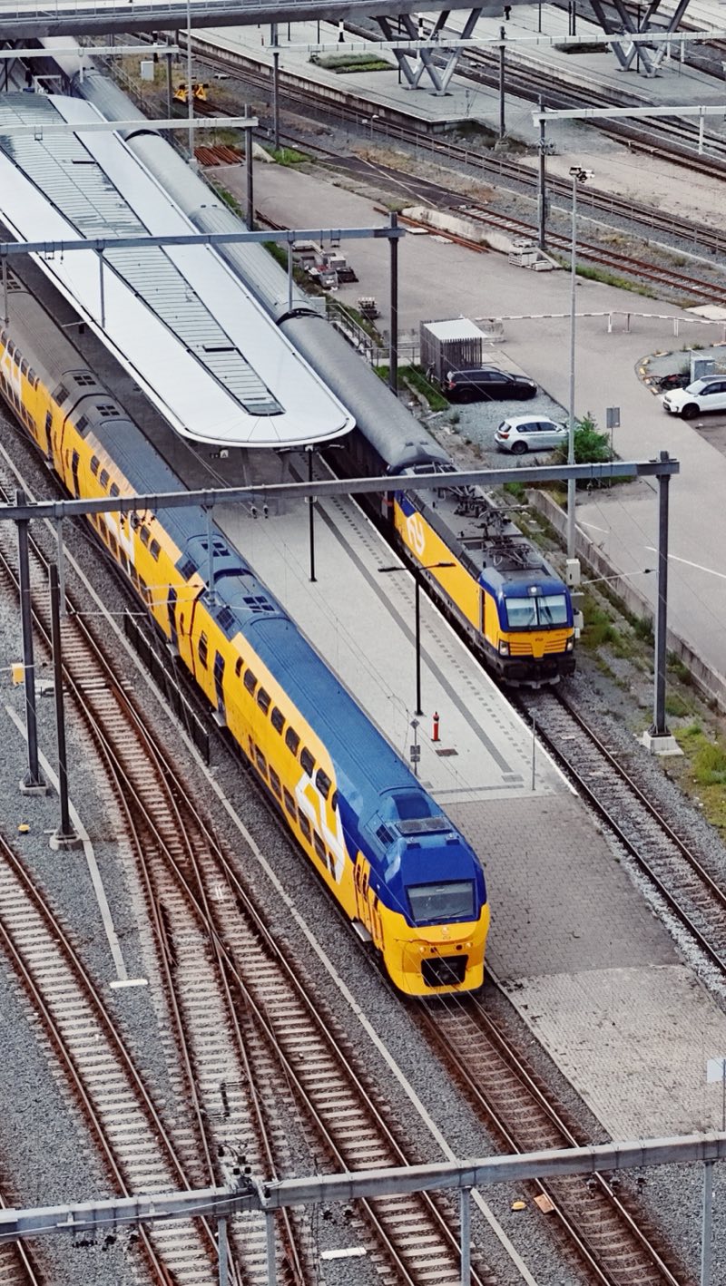 Yellow and blue double-deck trains at a station platform, seen from above.
